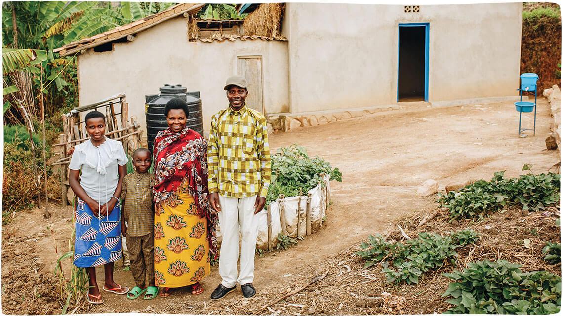 A Rwandan family with a mother, father, daughter, and son stand in front of their home and garden in Bwira, Rwanda