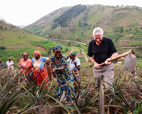 A Canadian businessman hoes in a pineapple field alongside female Rwandan farmers