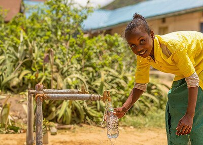 girl holding a clear bottle under a tap that is running clean water