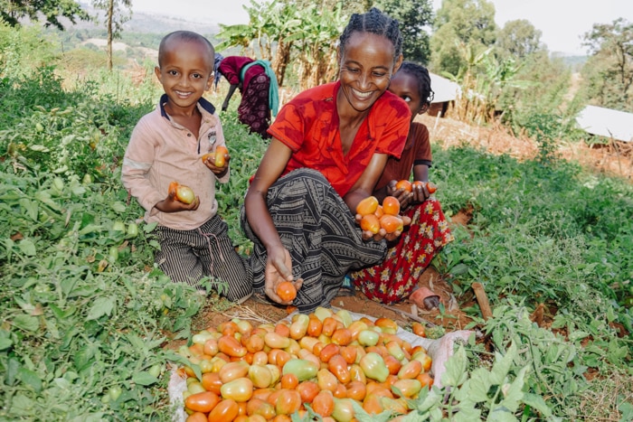 smiley woman and son holding tomatoes in a field