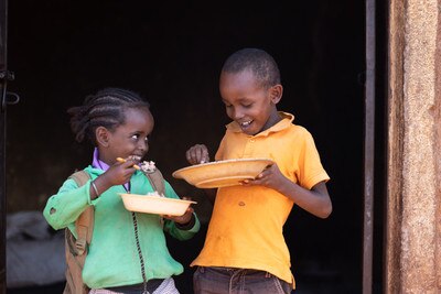 two smiling kids with a plate of food eating
