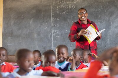 one teacher smiling with a book at their hands in a room full of children