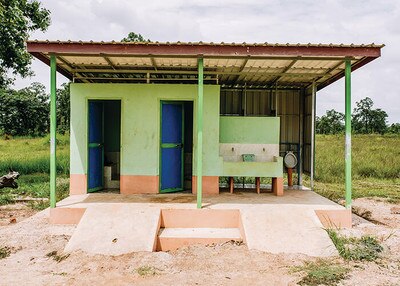 green building with two door for toilets, one external urinal, and two sinks, clean toilet