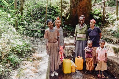 four woman and two girls getting water in a well