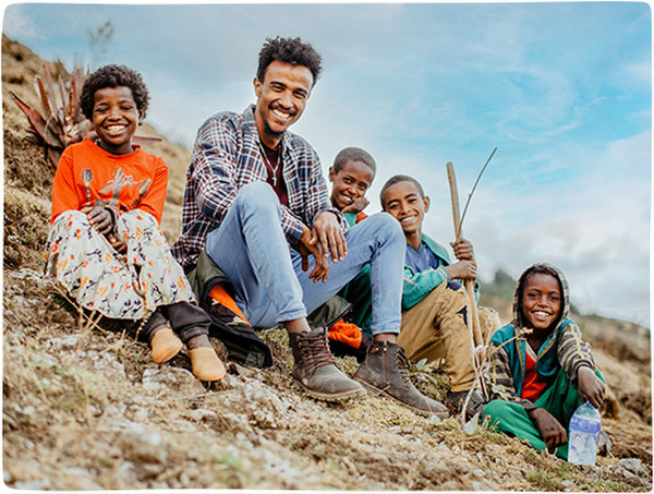 A group of four young Ethiopian children and a young adult smile sitting on a hillside in Sasiga, Ethiopia